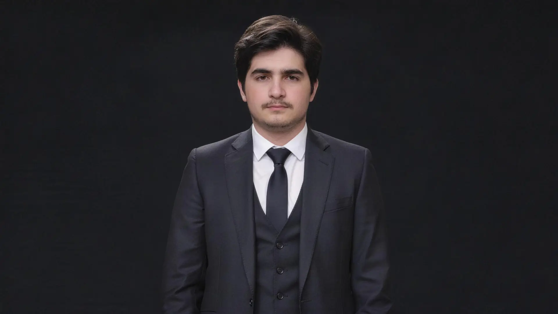 Koyu stüdyo fonu önünde, kameraya bakan takım elbiseli genç adam — Feterra Medya kurucusu.