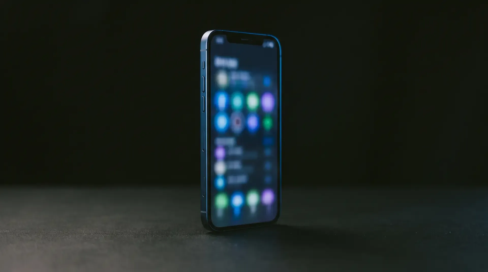 Koyu masada duran, ekranı bulanık arayüz ışığıyla parlayan telefon.